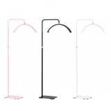 Three modern floor lamps with curved overhead arms and flat square bases, shown in pink, black, and white